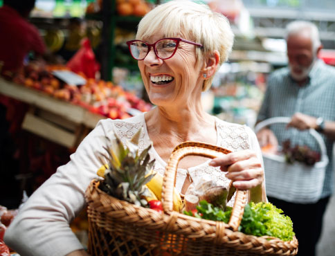 An older woman holding a basket of fresh fruits and vegetables